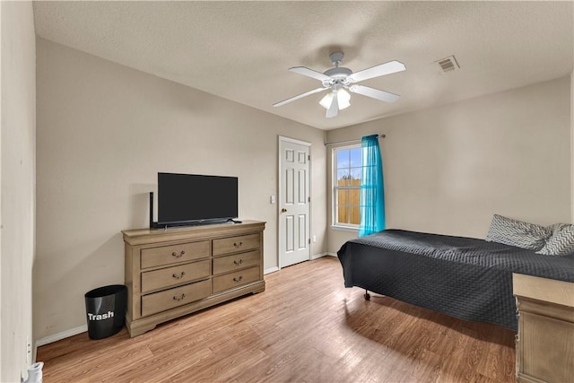 bedroom featuring light wood finished floors, visible vents, baseboards, a textured ceiling, and a ceiling fan