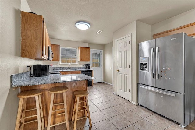 kitchen with a sink, stone countertops, stainless steel appliances, a peninsula, and light tile patterned floors