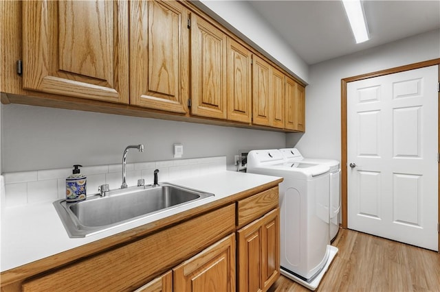 clothes washing area with separate washer and dryer, cabinet space, light wood-type flooring, and a sink