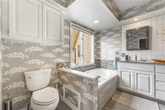 bathroom with toilet, wallpapered walls, vanity, and a garden tub