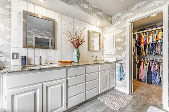 full bathroom featuring wallpapered walls, double vanity, a spacious closet, and a sink