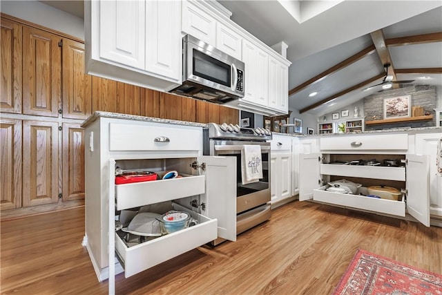 kitchen featuring light wood finished floors, vaulted ceiling with beams, appliances with stainless steel finishes, and white cabinetry