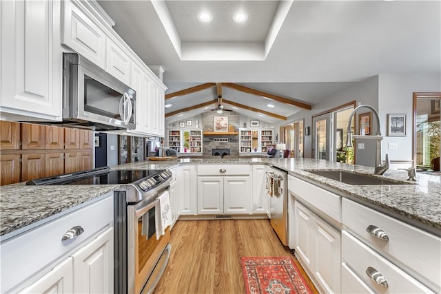 kitchen featuring lofted ceiling with beams, light wood-style flooring, a sink, stainless steel appliances, and white cabinetry