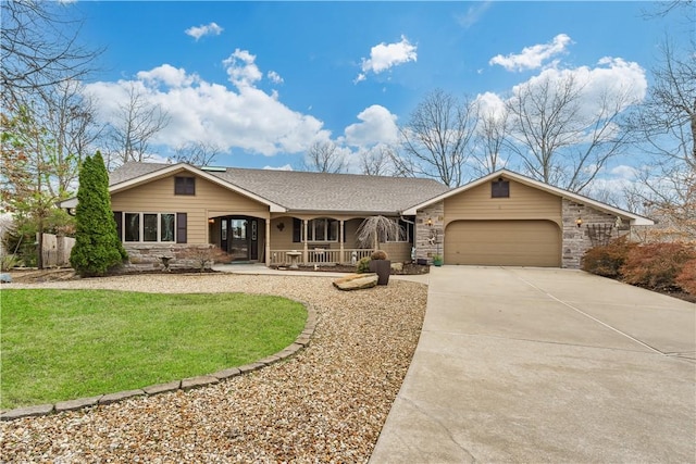 view of front facade featuring a front yard, covered porch, concrete driveway, a garage, and stone siding