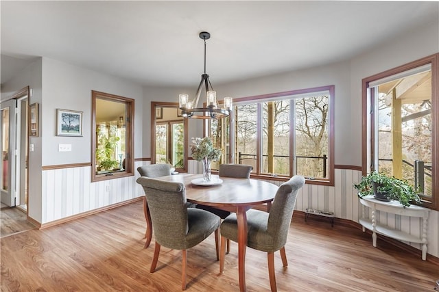 dining area with a wainscoted wall, a notable chandelier, and light wood finished floors