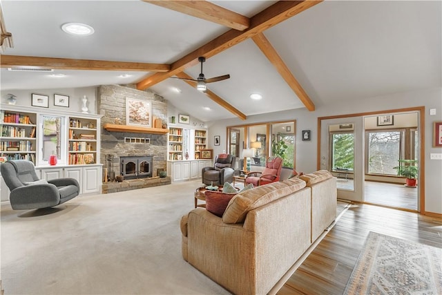 living area with a stone fireplace, lofted ceiling with beams, ceiling fan, and wood finished floors