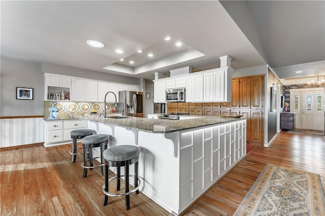 kitchen featuring light wood finished floors, open shelves, a sink, stainless steel appliances, and a raised ceiling