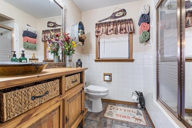 full bathroom with a stall shower, wainscoting, vanity, tile walls, and toilet