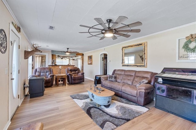 living area featuring ceiling fan, arched walkways, ornamental molding, and light wood-style floors