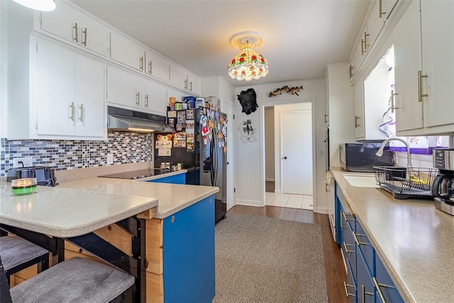 kitchen featuring under cabinet range hood, blue cabinetry, tasteful backsplash, and light countertops