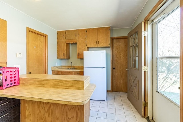 kitchen with a peninsula, light countertops, freestanding refrigerator, and a sink