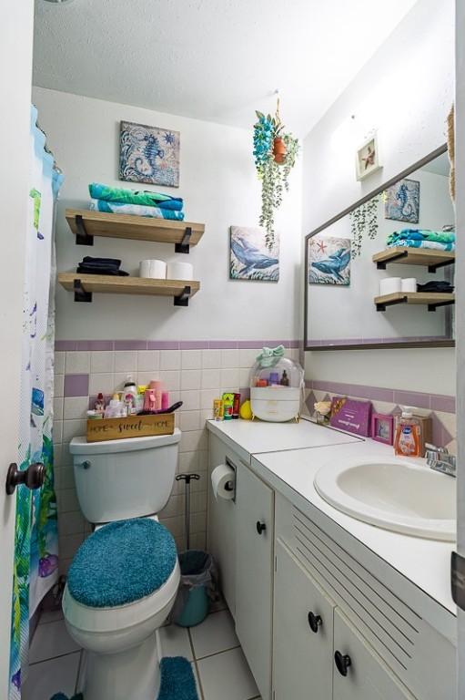 full bath with tile patterned flooring, tile walls, toilet, wainscoting, and vanity