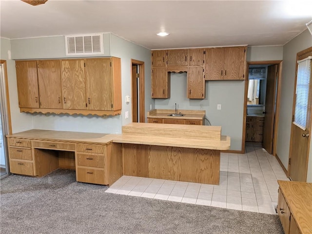 kitchen with built in desk, a sink, light countertops, a peninsula, and visible vents
