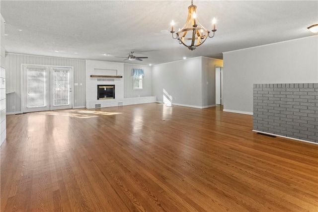 unfurnished living room with crown molding, baseboards, ceiling fan with notable chandelier, a fireplace, and wood finished floors