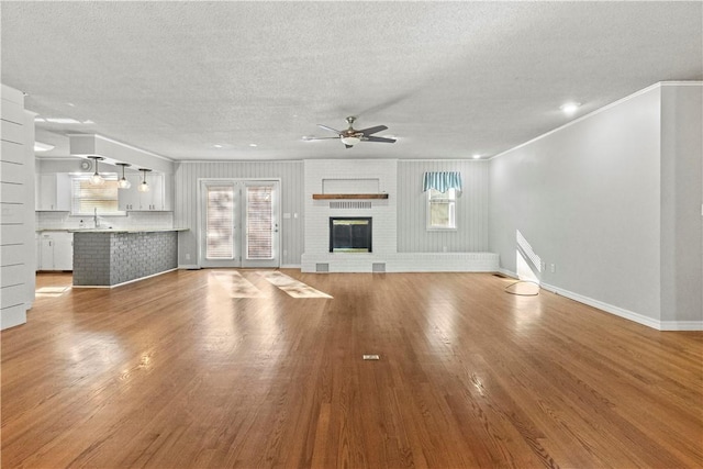 unfurnished living room with wood finished floors, a ceiling fan, baseboards, a fireplace, and a textured ceiling