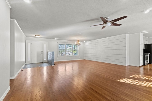 unfurnished living room with ceiling fan with notable chandelier, wood finished floors, baseboards, and a textured ceiling
