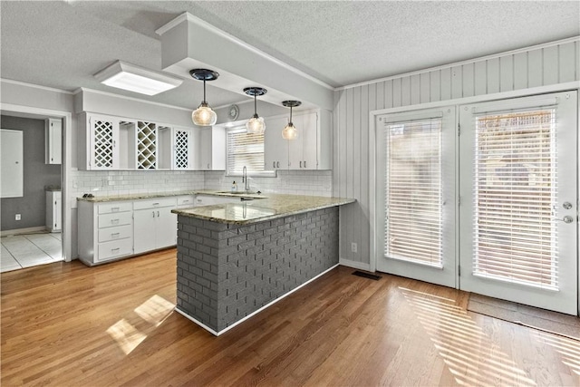 kitchen featuring a peninsula, white cabinets, light wood finished floors, and a sink