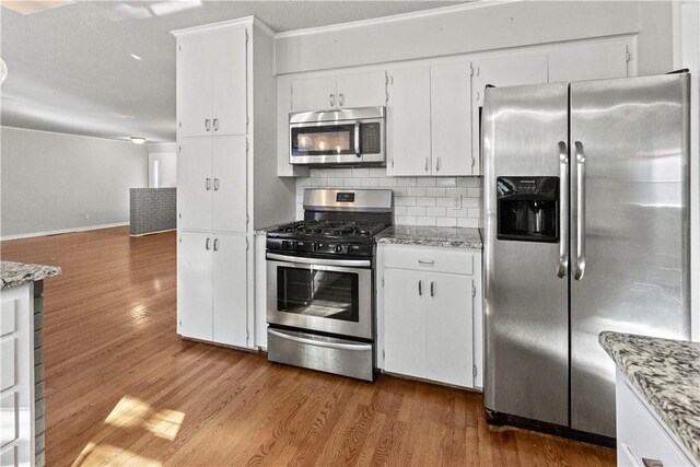 kitchen with light stone countertops, wood finished floors, white cabinets, appliances with stainless steel finishes, and tasteful backsplash