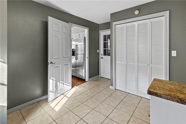 unfurnished bedroom with light tile patterned floors, baseboards, and stainless steel fridge with ice dispenser