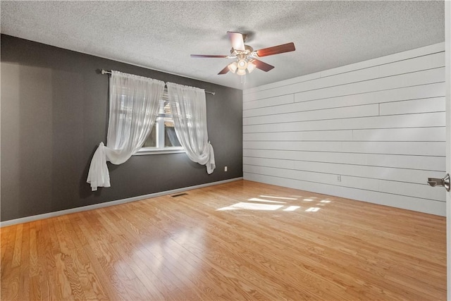 spare room with wooden walls, a ceiling fan, wood finished floors, visible vents, and a textured ceiling
