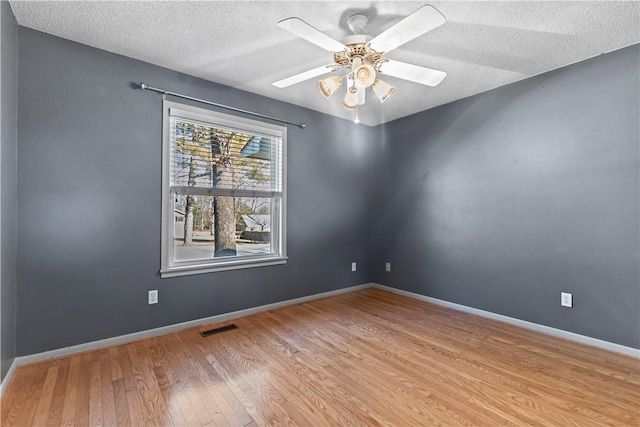 empty room featuring a ceiling fan, visible vents, wood finished floors, baseboards, and a textured ceiling