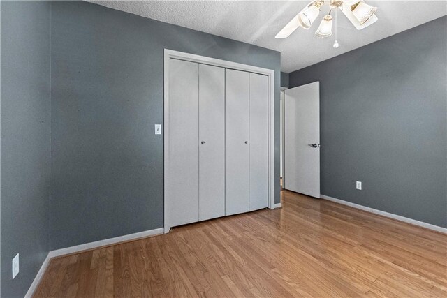 unfurnished bedroom featuring a ceiling fan, wood finished floors, baseboards, a closet, and a textured ceiling