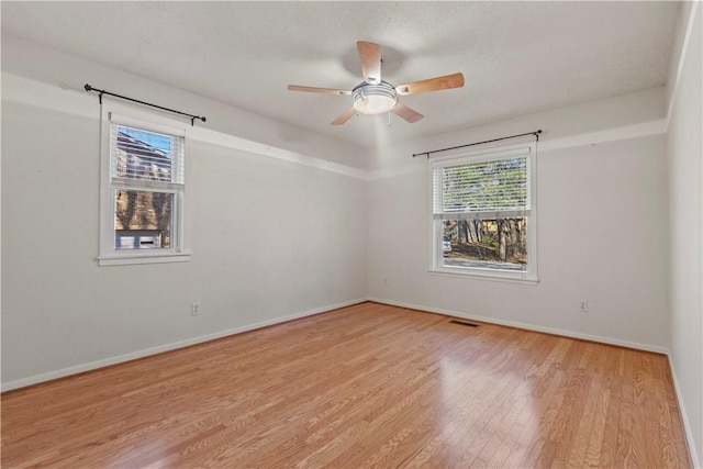 unfurnished room featuring a ceiling fan, visible vents, wood finished floors, and baseboards