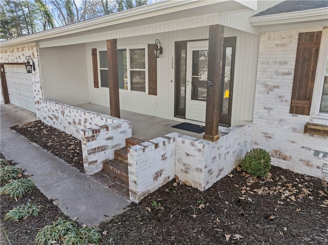 property entrance with a garage, brick siding, and covered porch