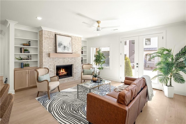 living room featuring a ceiling fan, built in features, light wood-style floors, a fireplace, and crown molding