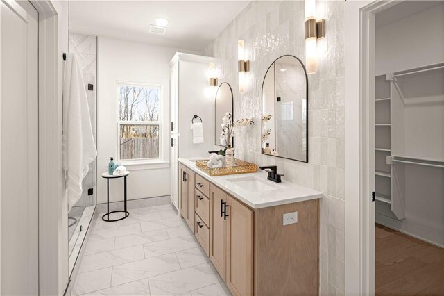 bathroom with a walk in closet, double vanity, marble finish floor, tile walls, and a sink