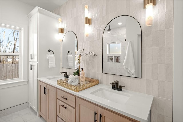 bathroom featuring double vanity, marble finish floor, tile walls, and a sink