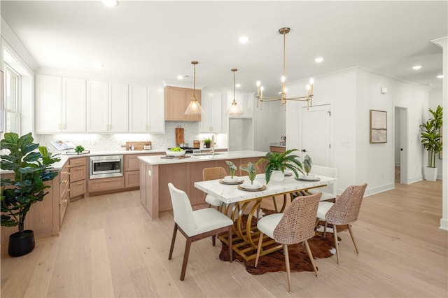 kitchen featuring light wood-style flooring, a kitchen island with sink, a sink, stainless steel microwave, and backsplash