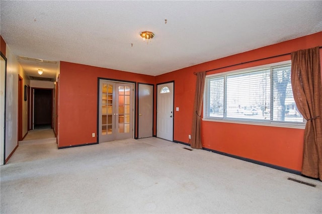 unfurnished room featuring visible vents, light carpet, a textured ceiling, french doors, and baseboards