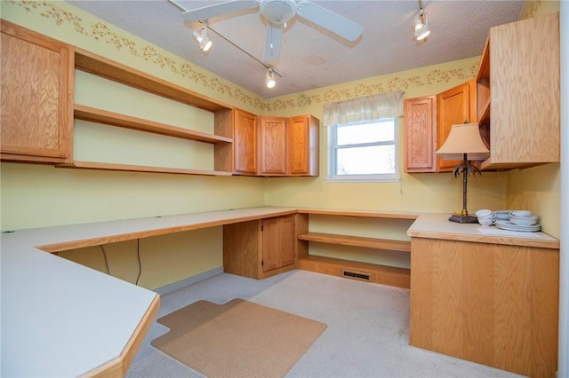 unfurnished office with a ceiling fan, visible vents, track lighting, built in desk, and a textured ceiling