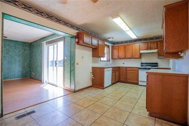 kitchen featuring visible vents, brown cabinets, under cabinet range hood, white dishwasher, and range