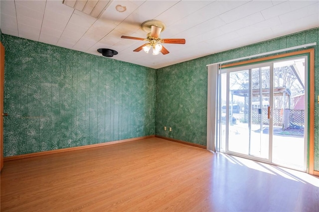 spare room featuring wallpapered walls, wood finished floors, baseboards, and ceiling fan