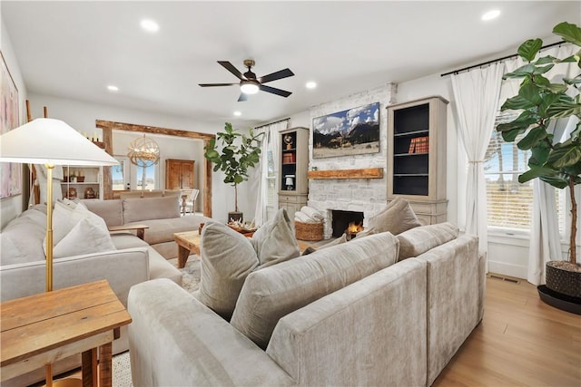 living area featuring visible vents, light wood finished floors, recessed lighting, a stone fireplace, and ceiling fan with notable chandelier