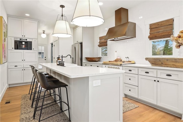 kitchen with visible vents, appliances with stainless steel finishes, light wood-style flooring, and wall chimney range hood