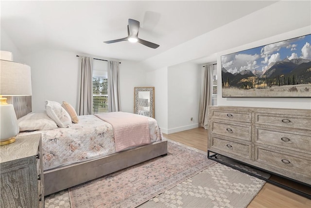 bedroom featuring baseboards, light wood-type flooring, lofted ceiling, and a ceiling fan