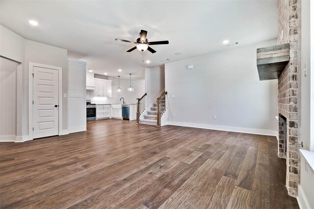 unfurnished living room featuring ceiling fan, a fireplace, dark wood finished floors, stairs, and recessed lighting