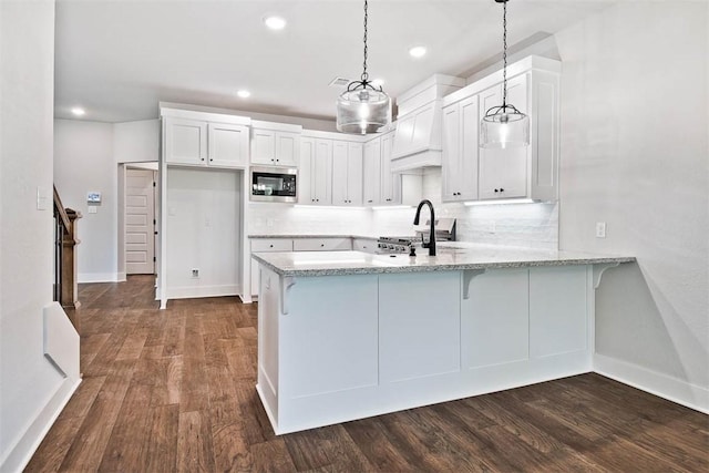 kitchen with white cabinets, light stone counters, a peninsula, stainless steel microwave, and baseboards