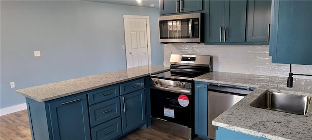 kitchen featuring appliances with stainless steel finishes, a peninsula, dark wood-style flooring, tasteful backsplash, and blue cabinets