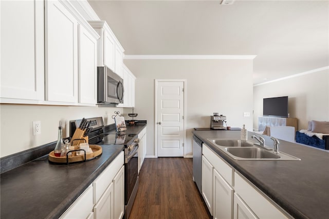kitchen with white cabinets, stainless steel appliances, dark countertops, ornamental molding, and a sink