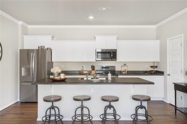 kitchen featuring white cabinets, stainless steel appliances, dark countertops, a sink, and a kitchen bar