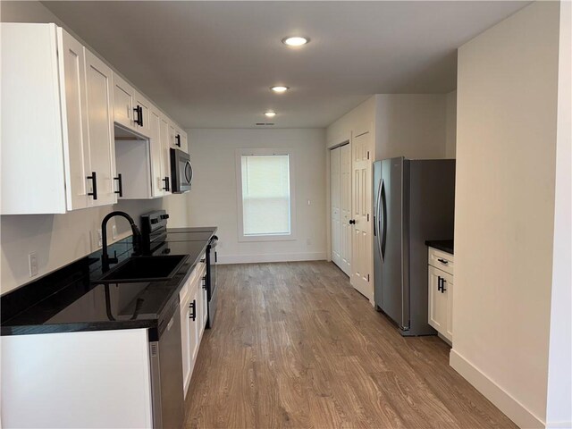 311 Douglas St, Berryville, AR 72616 - kitchen with dark countertops, appliances with stainless steel finishes, wood finished floors, white cabinetry, and a sink