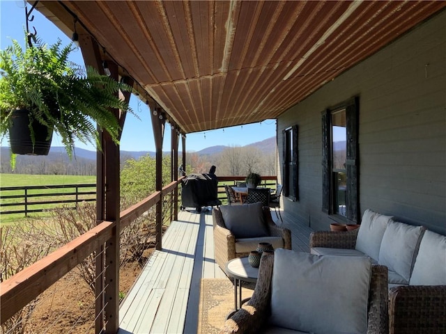 wooden deck with a rural view, an outdoor living space, and a mountain view