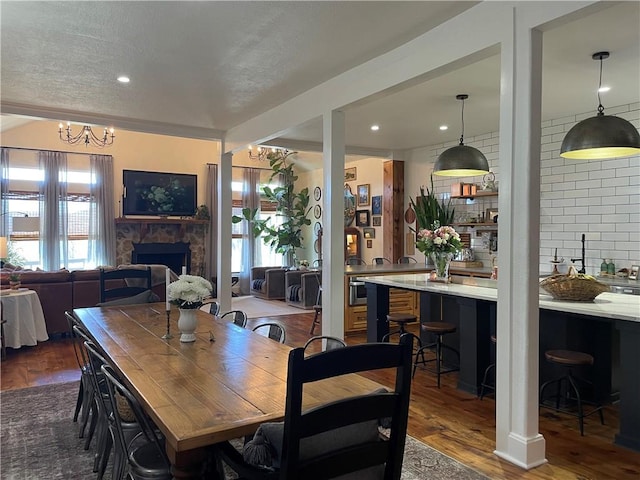 dining space featuring recessed lighting, dark wood-style flooring, a stone fireplace, and an inviting chandelier