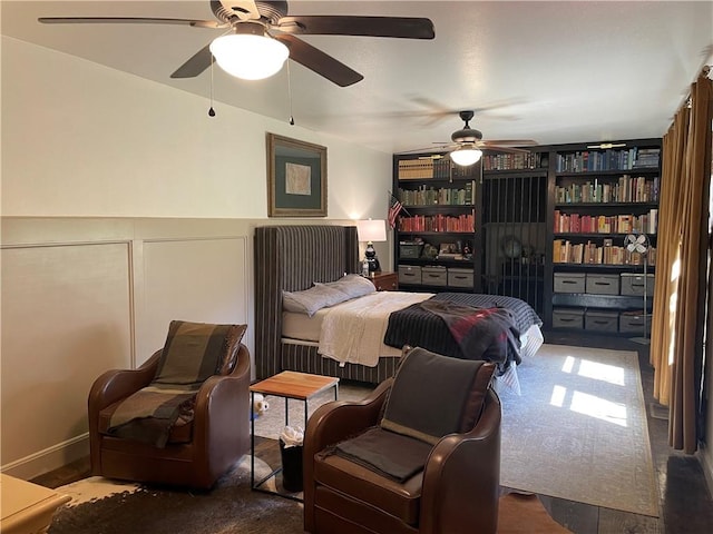 bedroom featuring a decorative wall, wainscoting, and ceiling fan
