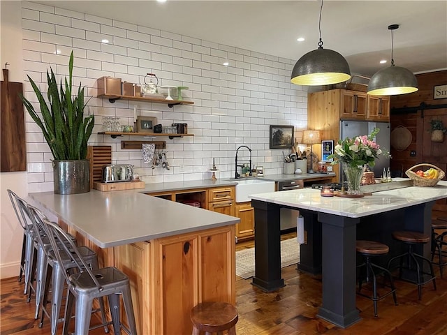 kitchen featuring tasteful backsplash, stainless steel fridge, light countertops, a kitchen bar, and a sink