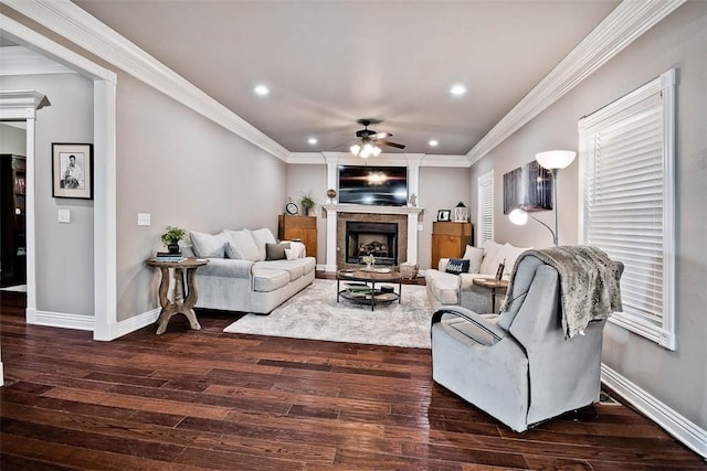living area with crown molding, a ceiling fan, wood finished floors, a fireplace with raised hearth, and baseboards